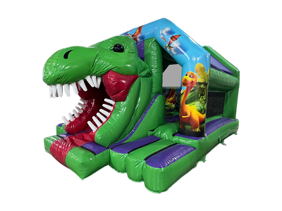 A green inflatable dinosaur-themed bouncy castle with a slide shaped like a dinosaur head, featuring white teeth, a red mouth interior, purple steps, and dinosaur illustrations on the side panels.